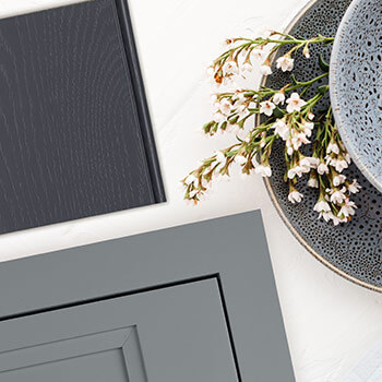 An inset cabinet door style on a quartz countertop with a gray painted finish paired with a dark gray-blue painted cabinet finish on oak wood. Kitchen and bath trends are featuring painted finishes with textured materials.