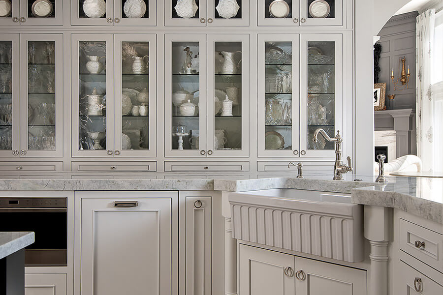 A classic traditional styled kitchen desing with off-white painted full overlay and inset cabinets A decorative farmhouse sink and a series of glass cabinets add a dash of elegance to the overall kitchen design. Learn about traditional interior design style and how to shop for traditional looking cabinets.