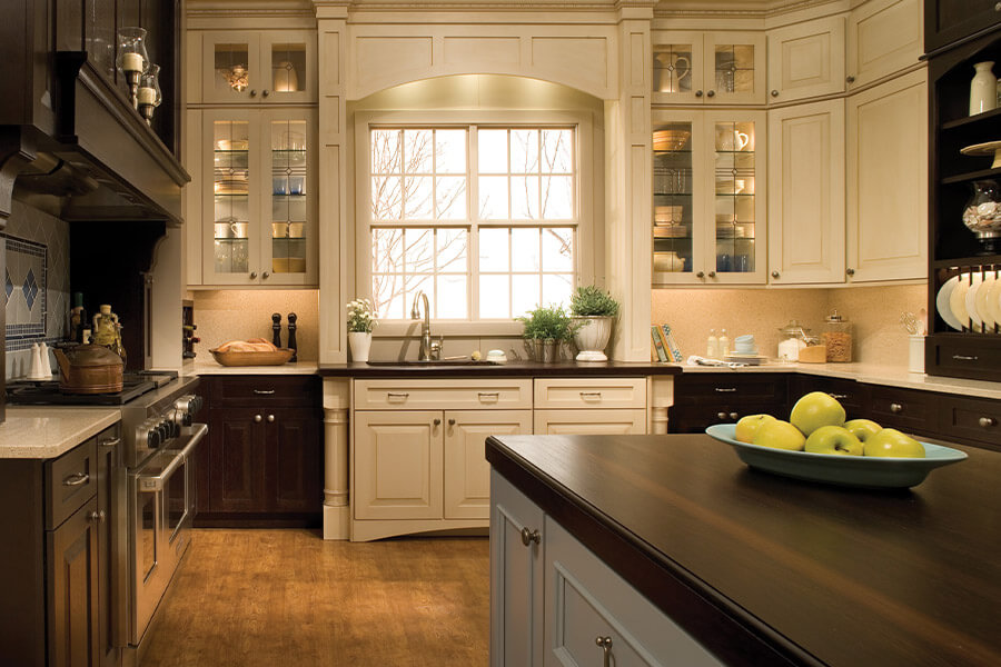This traditional styled kitchen remodel has a stunning kitchen sink window view. The kitchen island has a pale pastel blue painted finish while the perimeter of the kitchen has a combination of off-white painted wall cabinets with dark black stained base cabinets. Traditional styled architectural elements and cabinetry tend to be ornate and intricately detailed.