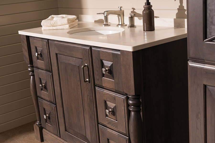 An ornate furniture style bathroom vanity with ornate turned post legs, raised panel cabinet doors, and a dark stained finish on cherry wood cabinets. Attention to detail is a strong characteristic of the interior design of this bathroom.