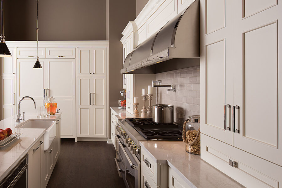 An elegant transitional style kitchen design with a large cooking area and stainless steel hood. The white painted cabinetry has a delicate flat panel door style that is casual and sophisticated. While there are hundreds of interior design styles to choose from, in general, they fall under a spectrum that consists of three primary design categories Traditional, Transitional, and Contemporary. This kitchen style lands right in the middle of the spectrum with it's very tansitional look.