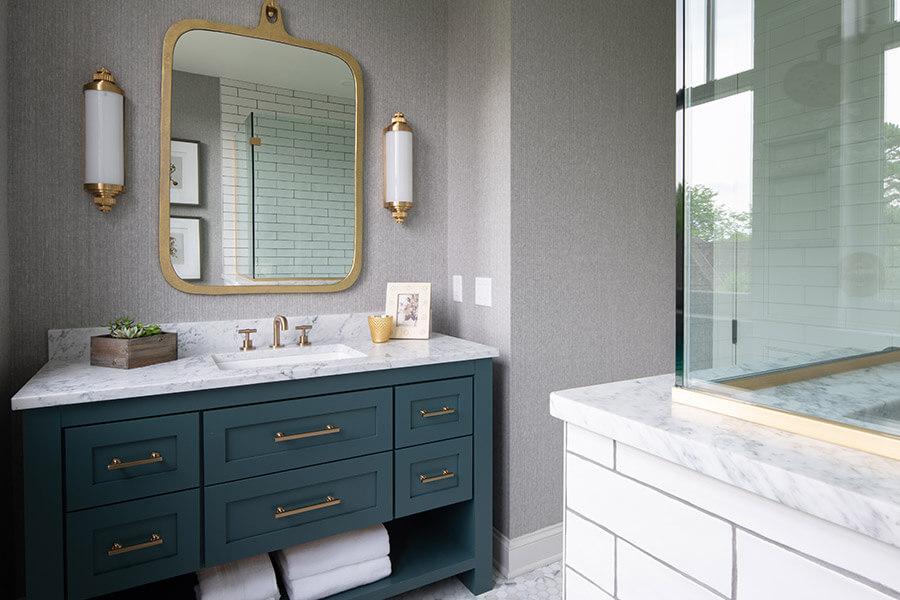 A nautical inspired transitional style bathroom design with a teal blue painted furniture style vanity. Brushed brass hardware and vanity mirror accent the space. With Transitional being between Traditional and Contemporary, you’ll find many styles under this design category including; Coastal, Modern Farmhouse, and Shaker.