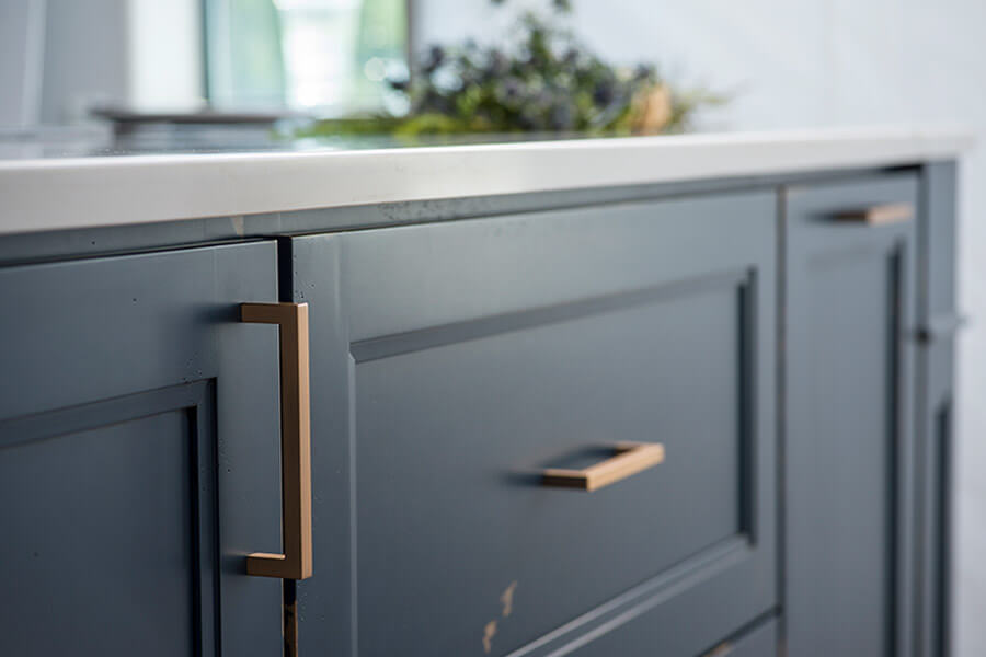A kitchen island with a distressed painted finish in a trendy navy blue color. Shaker cabinet doors have a delicate detailed profile.