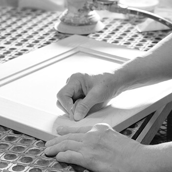 Here a cabinet maker is carefully hand-sanding the edges of a cabinet door to prepare it before it gets the finish applied to the surface.