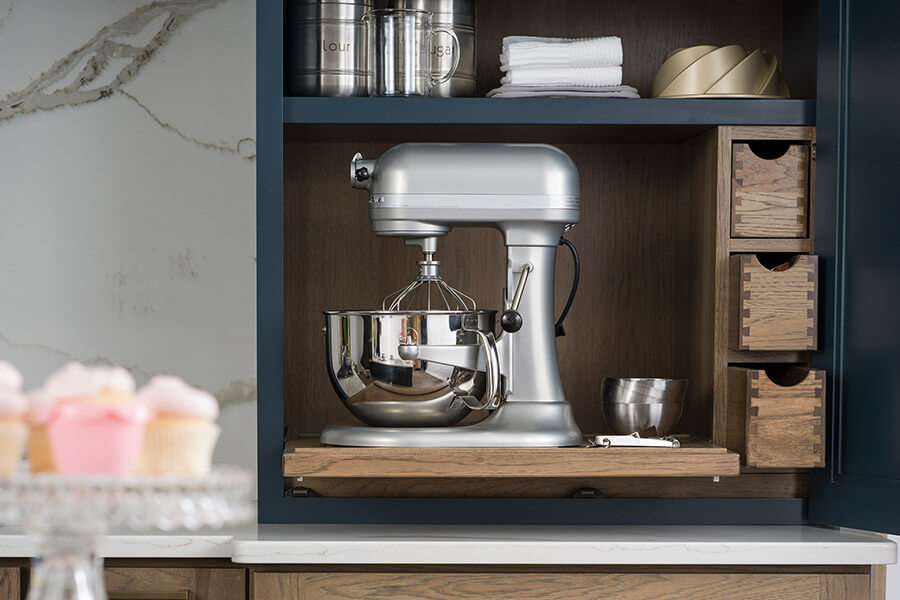 A baking center larder and pantry cabinet with a kitchen aid mixer on a pull-out shelf creates a balanced work zone for a baking center. Prepare for baking projects with an area dedicated to all the tasks.