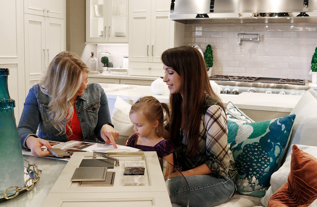 A kitchen designer working with a homeowner and her daughter to plan the storage solutions in a remodel project using Dura Supreme Cabinetry.