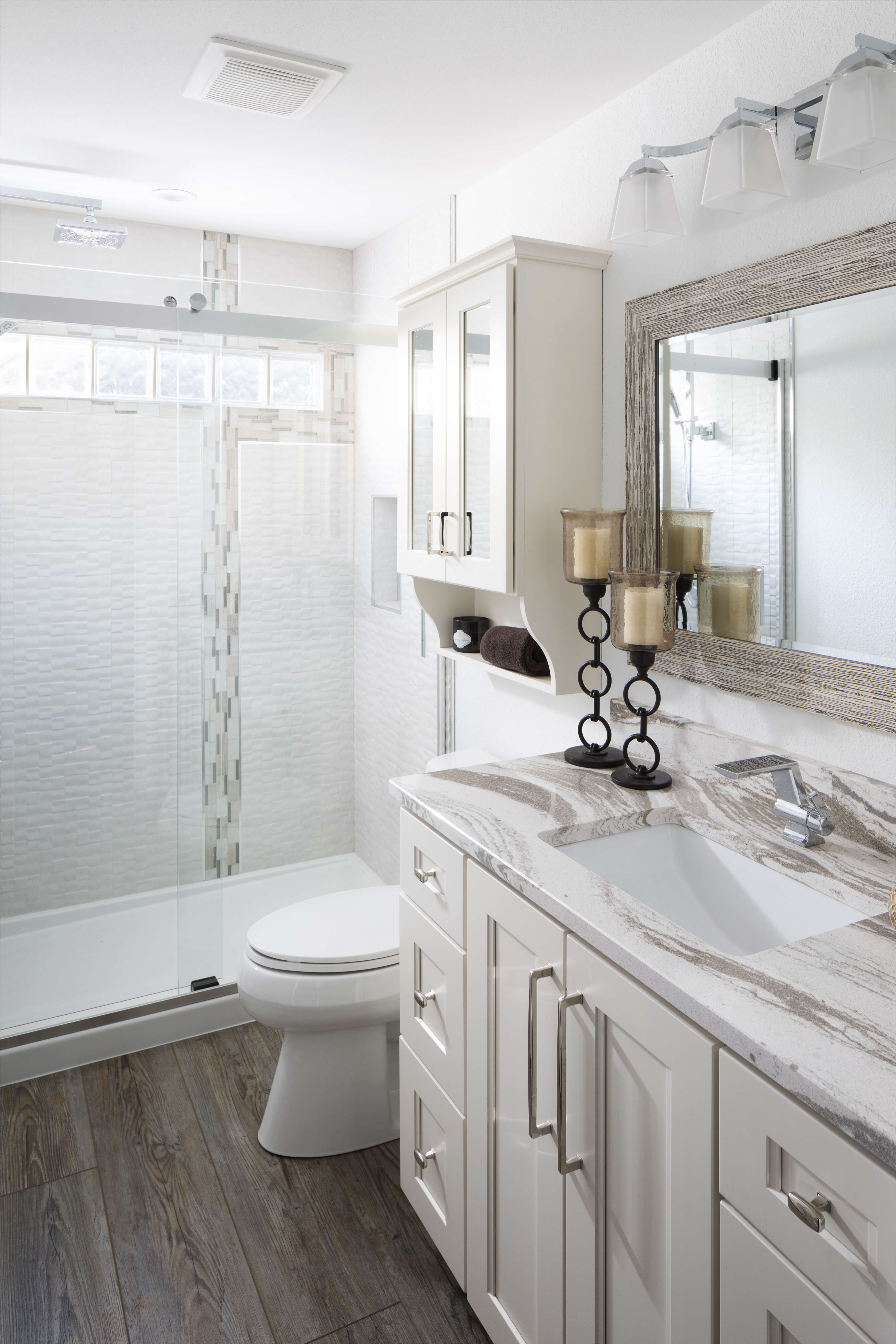 A newly remodeled bathroom with whote painted cabinets and mirrored cabinet doors.