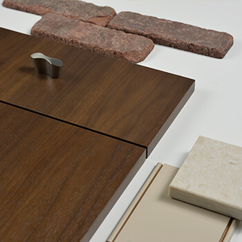 An industrial style kitchen design concept featuring a warm stained wood cabinet door with a brick backsplash and an off-white painted cabinet finish sample from Dura Supreme Cabinetry.