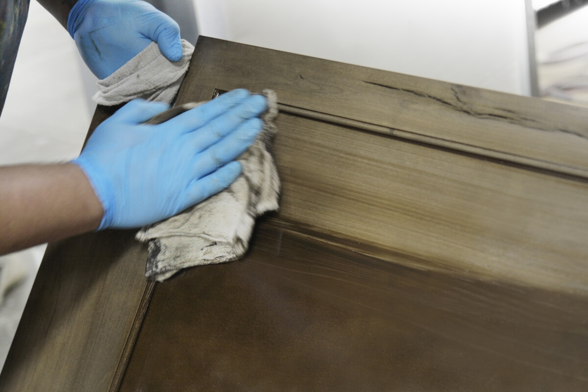 Close up of a cabinet maker and finish artisan hand wiping a stain and glaze finish on a wood cabinet door. Made in America cabinetry.