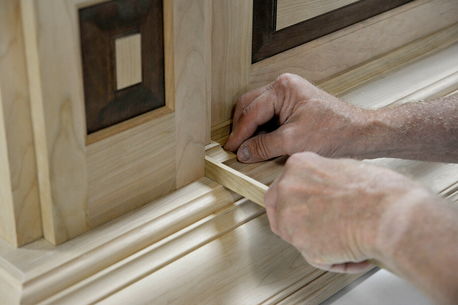 A craftsman working on the molding details to a kitchen wood hood inside the Dura Supreme Cabinetry factory in the USA.
