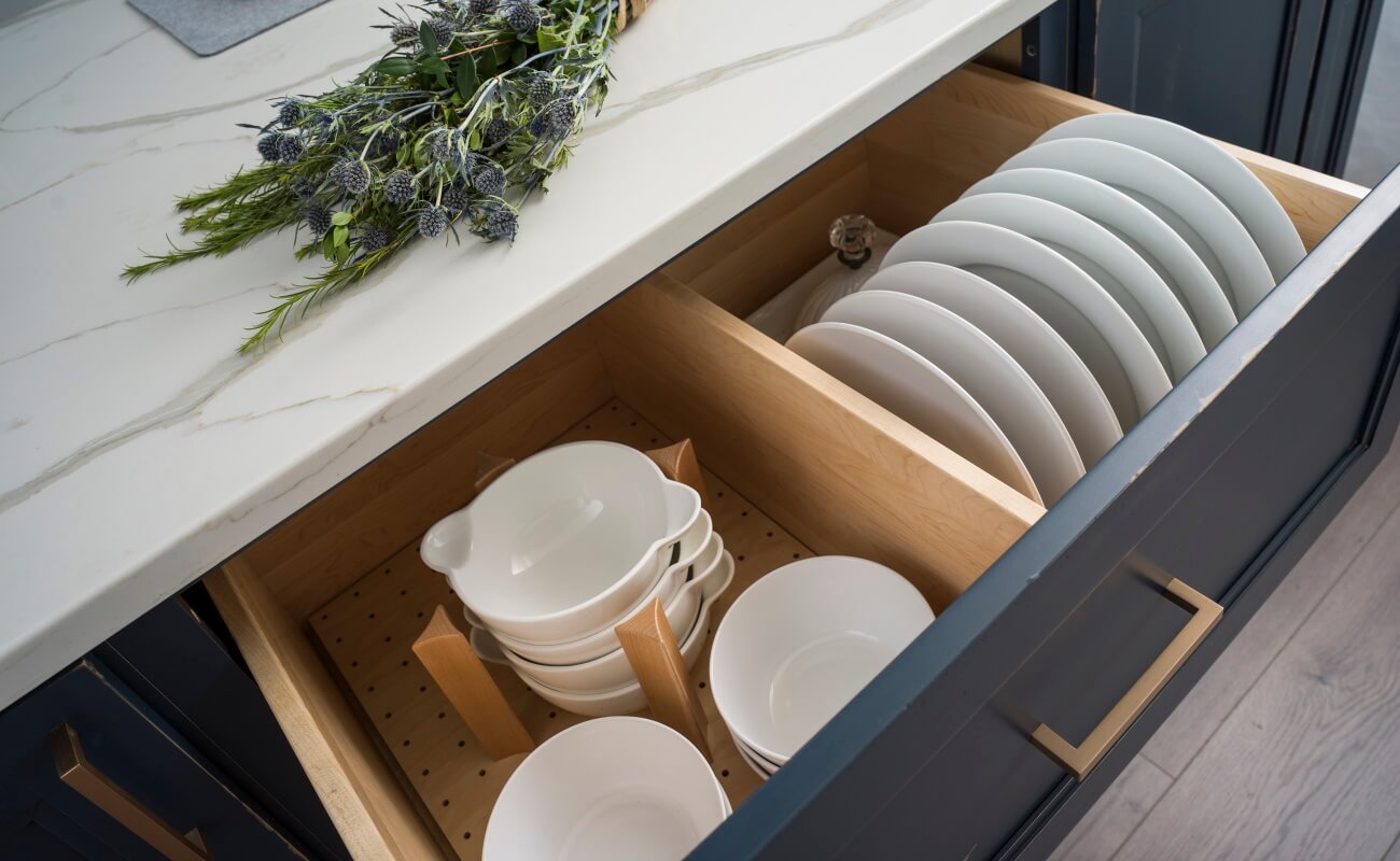 A kitchen drawer with a dishware and plateware storage and organizing accessories in a blue and white kitchen remodel.