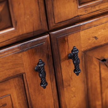 A close up of rustic wood cabinets with a patina finish and traditional raised panel cabinet doors.