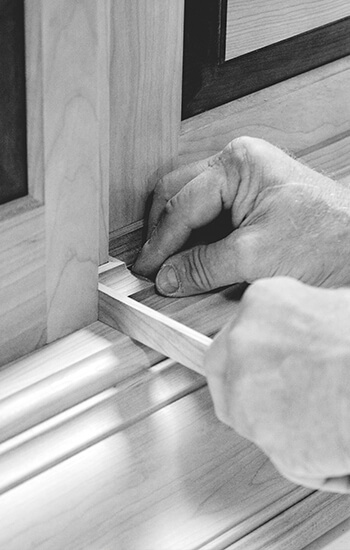 A craftsman's hands working on the molding details of a custom wood hood. This cabinet maker is hard at work crafting semi-custom and custom cabinets at the Dura Supreme Cabinetry factory in Minnesota, USA.
