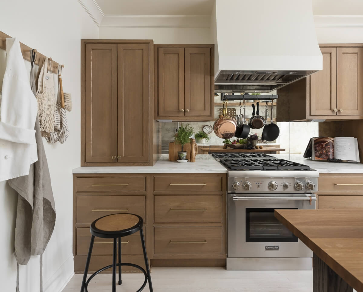 A straight on view of the kitchen remodel with light stained wood cabinets, white countertops, white painted wood hood, and dramatic mirror backsplash.