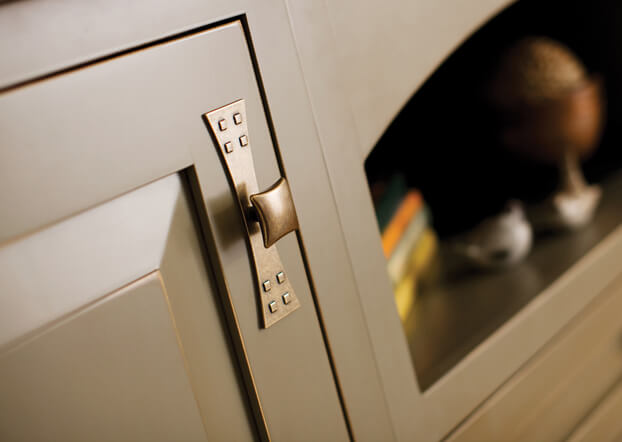 Dura Supreme's Lancaster – Inset door style in a custom olive green Rub-Thru Paint/Glaze finish. A close up of a craftsman style kitchen island with distressed green painted finish and bronze arts & crafts styled cabinet knob with backplate.