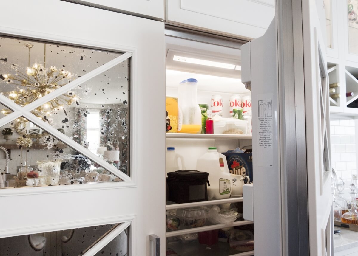 A refrigerator with mirrored cabinet appliance panels. Close up of the large kitchen appliance with cabinetry paneling.