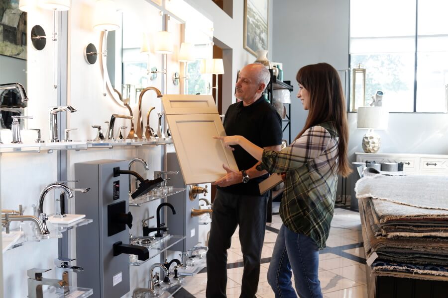 A customer talking to a designer at a kitchen & bathroom showroom looking at a sample of a cabinet door.