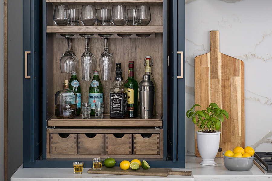 All the supplies, glassware, and tools for a home bar are hidden away in this countertop sitting larder cabinet. Hidden countertop storage is a growing trend in kitchen designs to help keep countertops clutter-free.