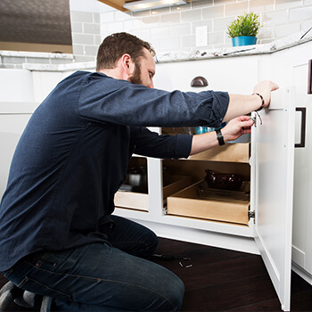 A homeowner making adjustments to the cabinet doors in his kitchen. Learn how to adjust and install Dura Supreme Cabinetry.