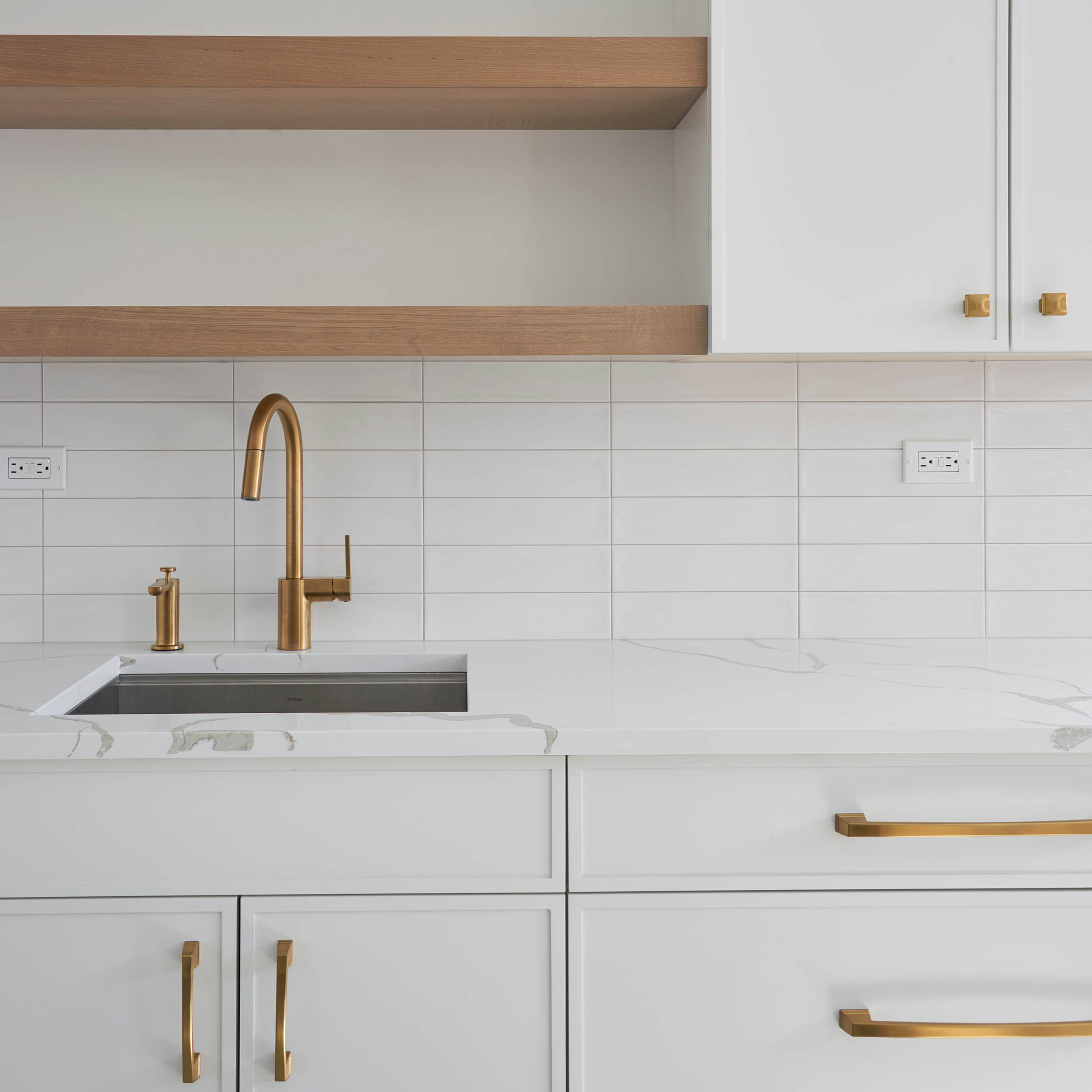 A white on white kitchen with Scandinavian style featuring white painted cabinets and white tile backsplash with light wood floating shelves above the kitchen sink.