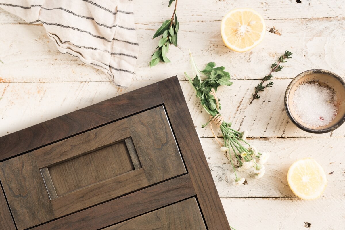 A beautiful inset cabinet door style shown in a medium, true-brown stain color on cherry wood is shown in a flat lay format over some off-white painted wood planks.