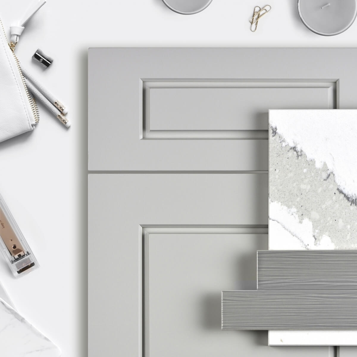 A flat lay showing a kitchen design mood board with an all gray color palette using a modern raised panel door with a gray painted finish as well as gray and white tiles and countertop samples.