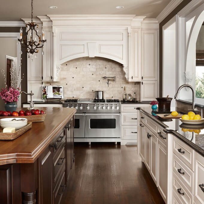 A traditional white kitchen with a grand, elegant wood hood over a double-wide range.