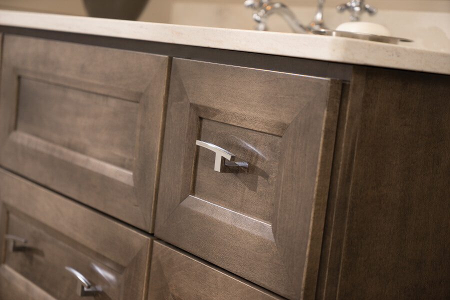 Learn how to Clean & Care for Your Dura Supreme Cabinetry with this cleaning and care guide. Here is a close up of a wood vanity cabinet with a gray-brown stained finish and a beveled flat panel door style.