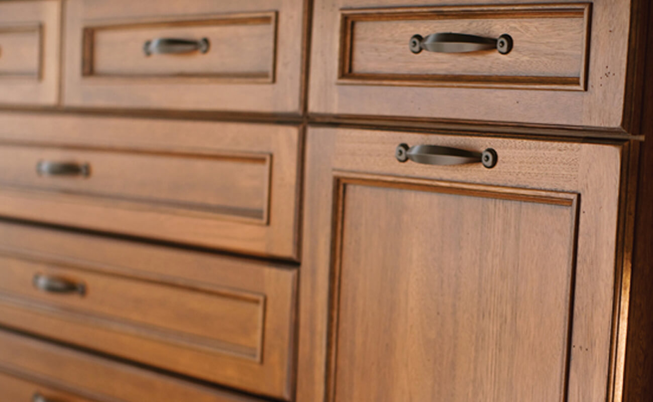 A close up of wood cabinets with a rich, medium stain color in a traditional style kitchen.