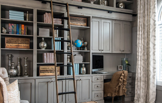 A rustic shabby chic styled living room with floor to ceiling bookcases, a rolling ladder, and a buit-in home office desk.