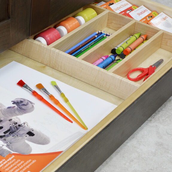 A toe-kick drawer with divided storage for kids school supplies for a homework station in the kitchen.