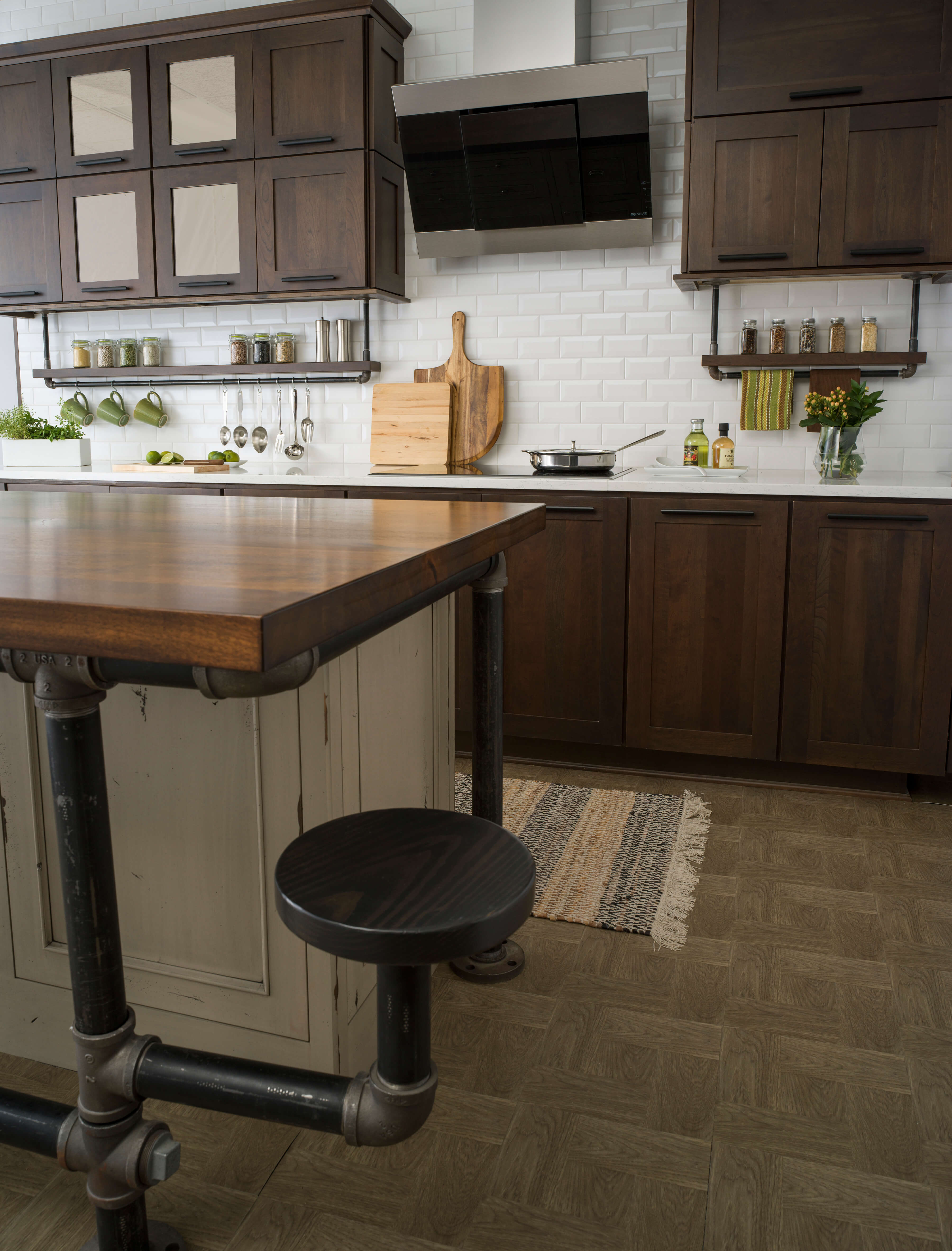 An industrial style kitchen remodel with modern and rustic cabinets. The distressed painted kitchen island has kitchen island stool stand made of pipe materials. Pipes are also used to accent the floating shelves below the wall cabinetry for displaying spices and hanging everyday cooking utensils.