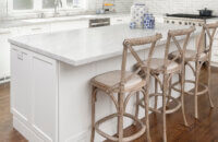 A white kitchen island with a white marble countertop and comfortable bar stool seating for three people.