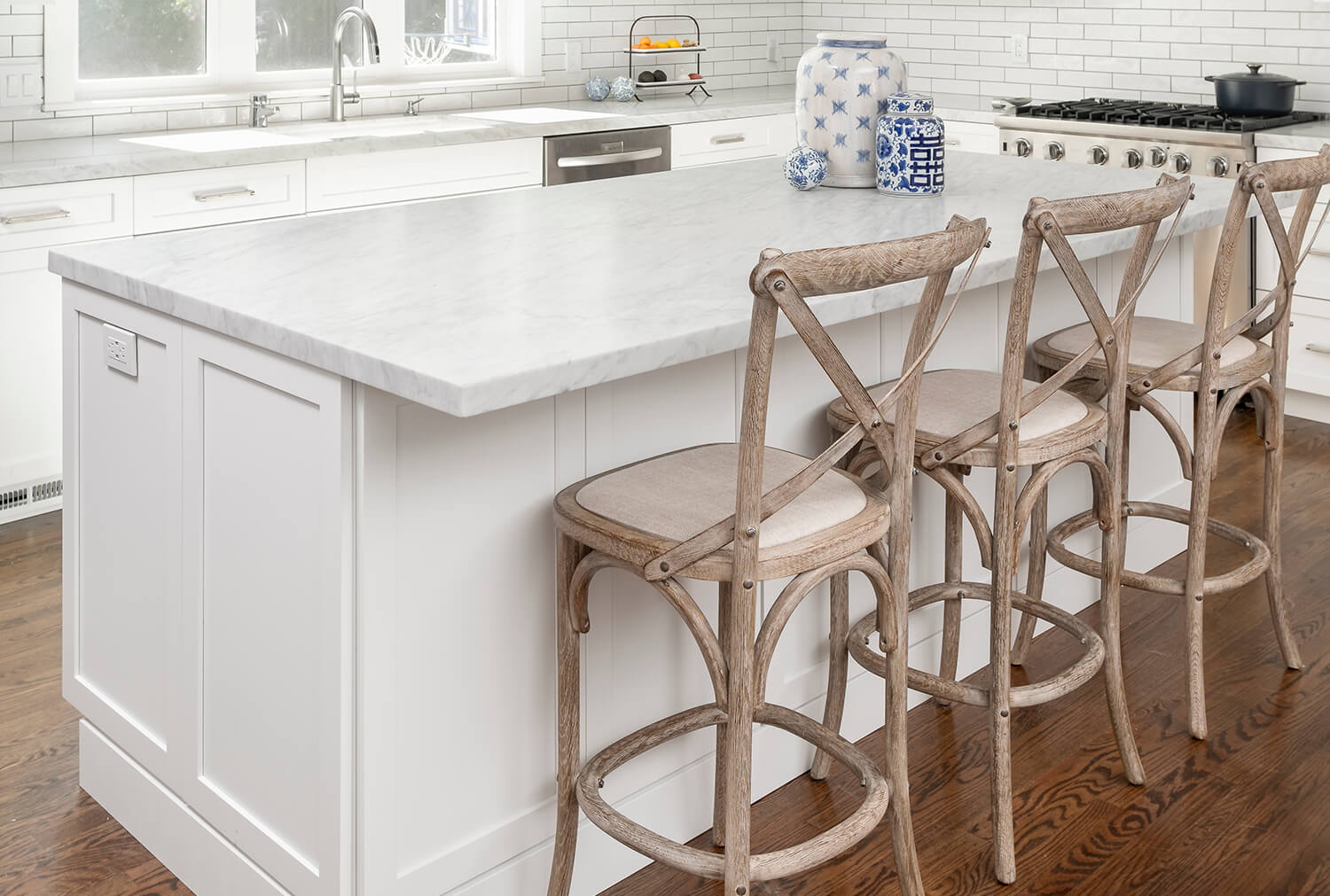 A white kitchen island with a white marble countertop and comfortable bar stool seating for three people.