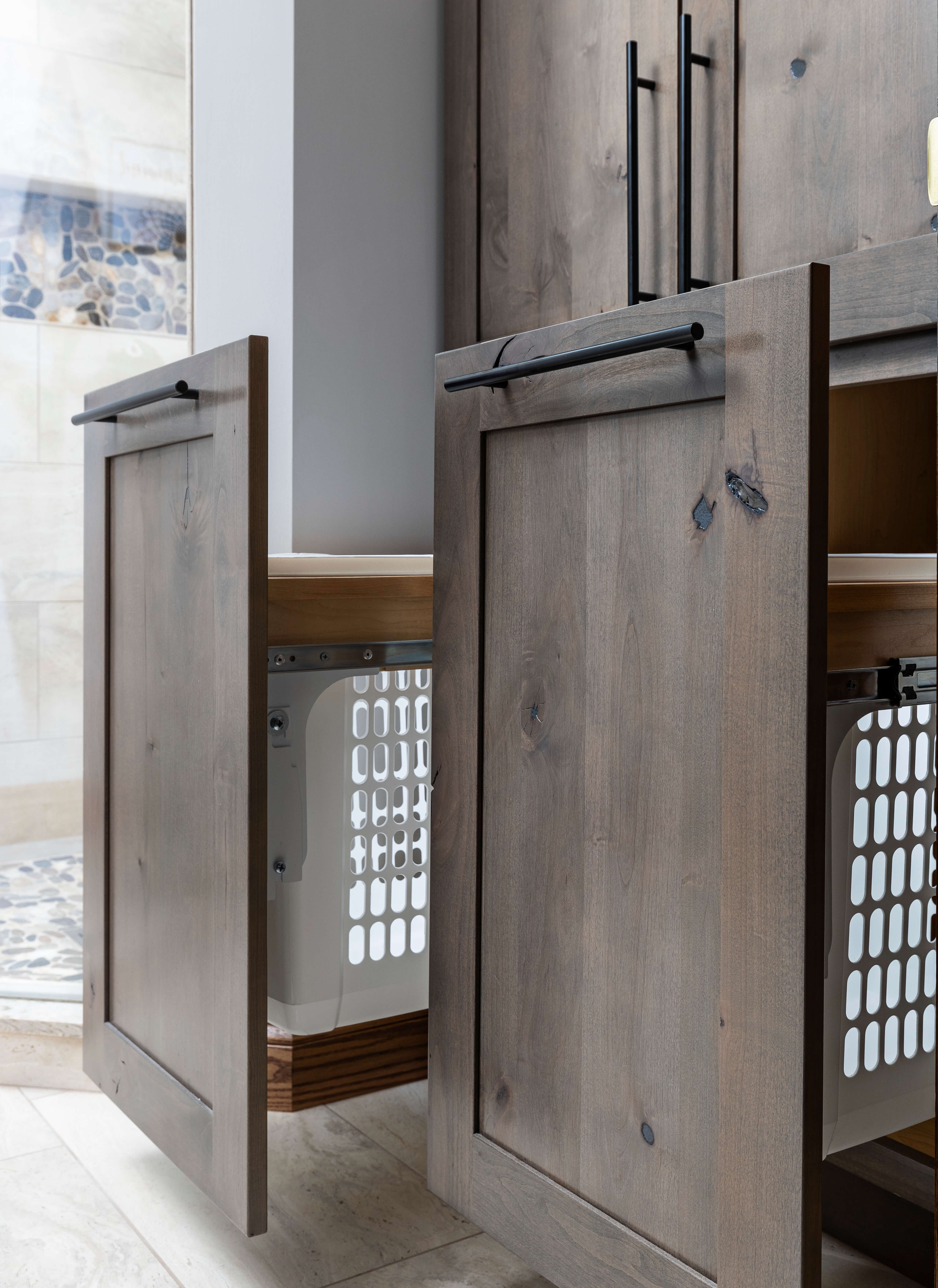 Two pull-out laundry hamper cabinets in a rustic knotty alder cabinet.