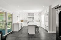 An all white kitchen with white cabinets, counters, and backsplash with a unique mix of metal finishes including brass cabinet hardware and stainless steel appliances.