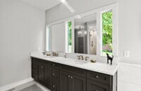 This black and white master bathroom has natural light pooling through the windows behind the vanity mirrors and a dark gray painted vanity.