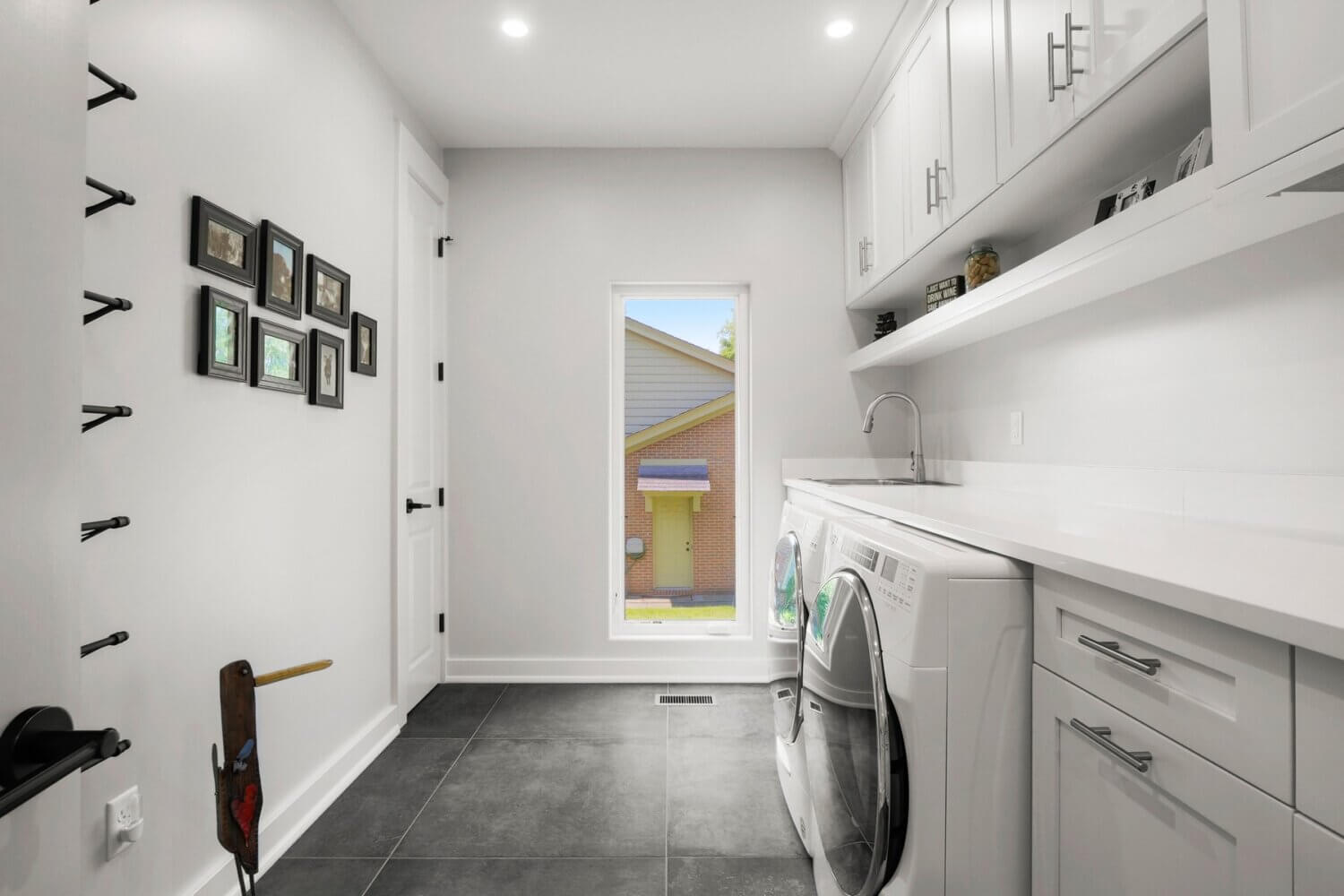 An all-white and bright laundry room with simple, sophisticated cabinets from Dura Supreme Cabinetry in a white painted finish. Dark gray tiles on the floor add contrast to the space.