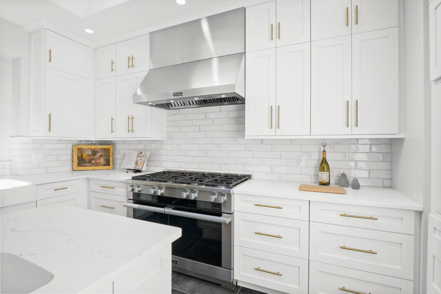 An all white kitchen with shaker cabinetry from Dura Supreme Cabinetry, brass hardware, and stainless steel appliances.