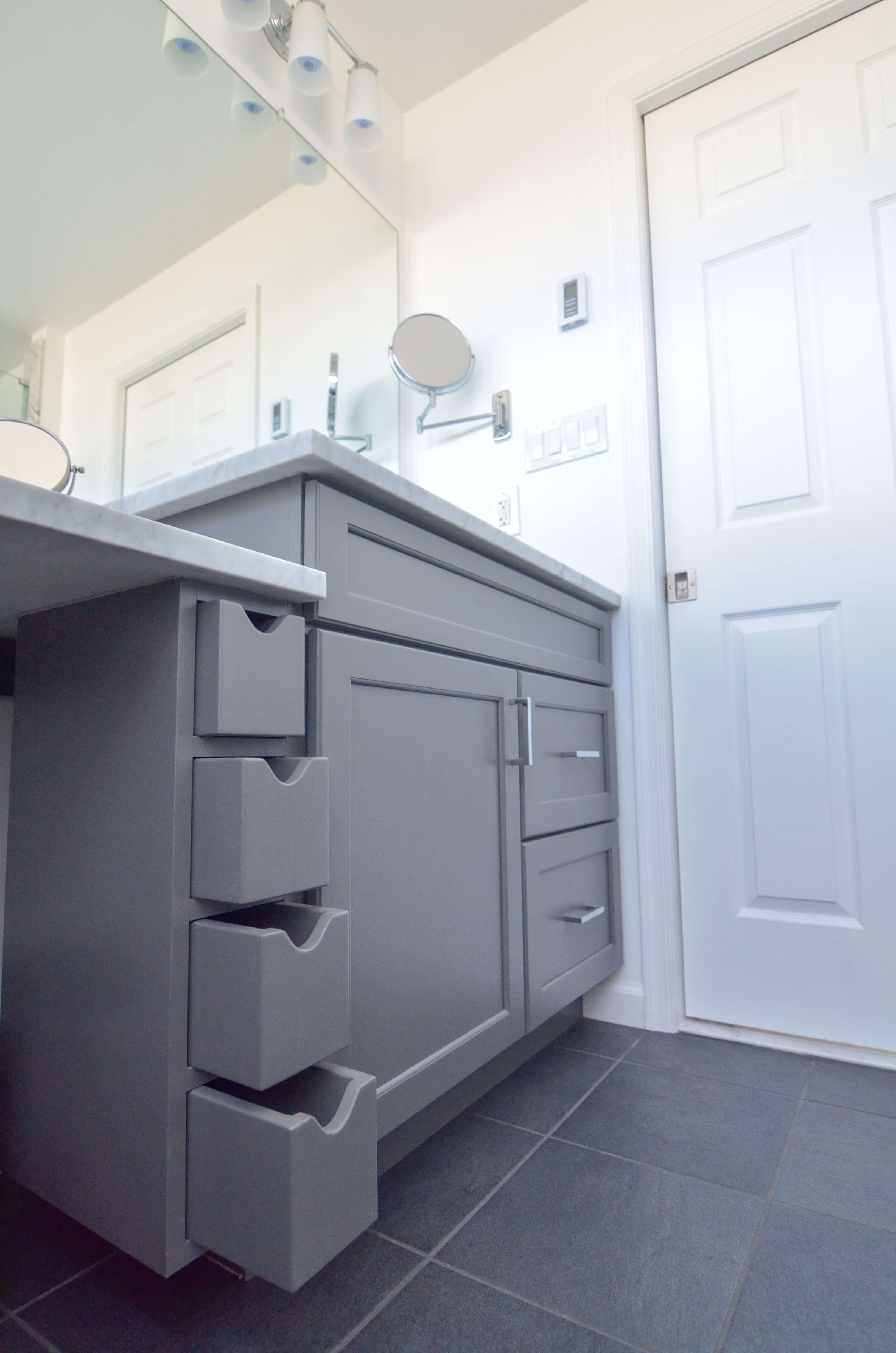 A close up of a dark gray painted vanity with a vertical row of apothecary drawers for storing organized cosmetic supplies.