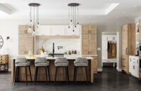 This kitchen has an American take on Scandinavian interior design style. The design features the slab Dash cabinet door style with wood plank-like details in a rustic oak texture mixed with a shaker door style in white paint. This kitchen island offers seating for four plus a kitchen sink across from the cooktop.