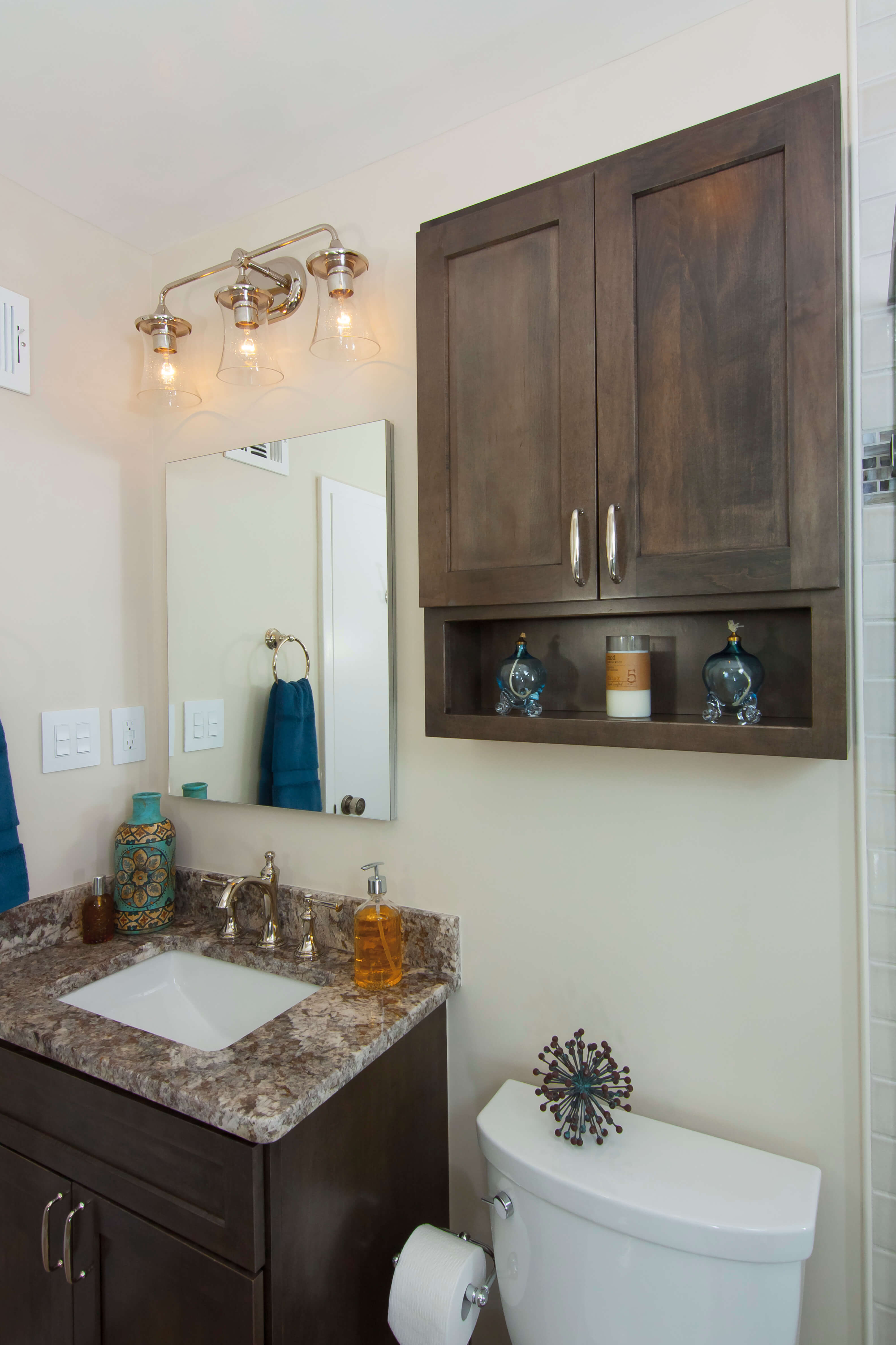 A small bathroom with dark stained wood cabinets for the vanity and matching small wall cabinet over the toilet.