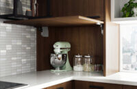 A counter-sitting cabinet in a modern city kitchen has a lift-up cabinet door that reveals the hidden small countertop appliances and supplies.