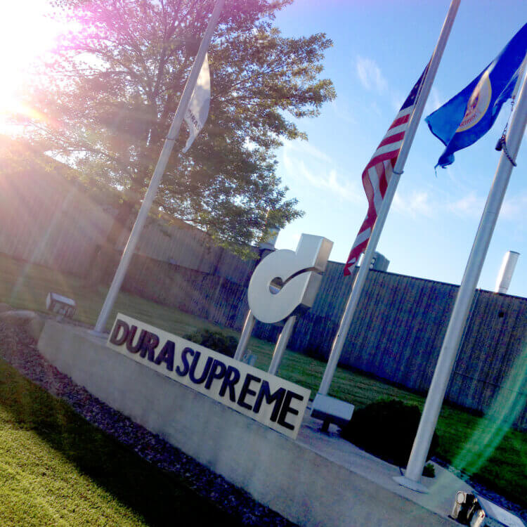 The exterior of Dura Supreme Cabinetry showing the sign with their logo and flags.