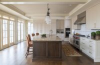 A classic traditional styled kitchen design with a dark stained kitchen island with countertop seating and white painted cabinets. A wall of windows brings in lots of natural light.