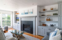 A living room with a full wall of gray built-in bookcase cabinets centered around matching gray fireplace mantel custom crafted by Dura Supreme.