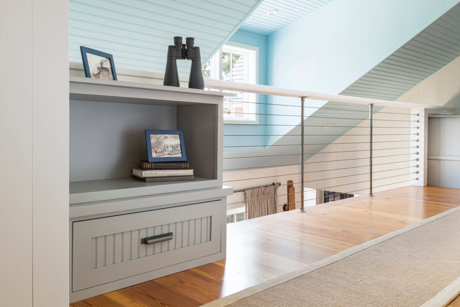 A close up of a small built-in cabinet with a cottage style and gray painted finish in a lofted hallway of a beach cottage home.