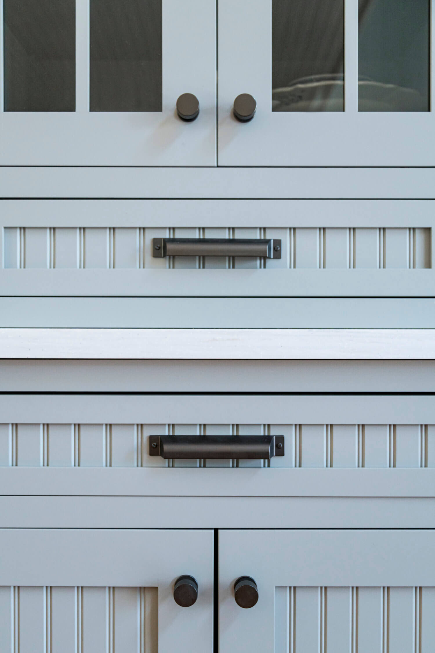 A close up of gray painted kitchen cabinet doors and drawers with a cottage bead board panel and shaker style.