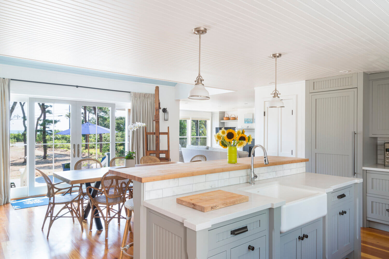A look over the kitchen peninsula into the dining room space of a cottage style kitchen with gray inset cabinets.