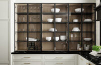 Glass cabinet doors with black metal door frames on white painted inset cabinets with a white oak cabinet interior, a skinny shaker style, and brass hardware.